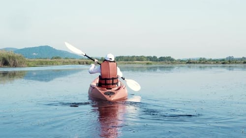 Back young adult woman paddling kayaking canoe on a lake on summer day