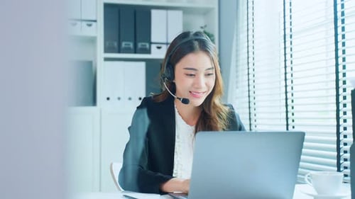 Asian business female call center wear headphone and talk to customer in office workplace.