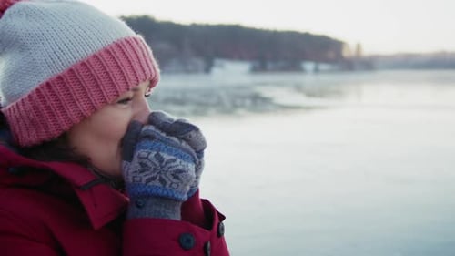 Woman Warming Hands By Frozen Lakeside in Winter