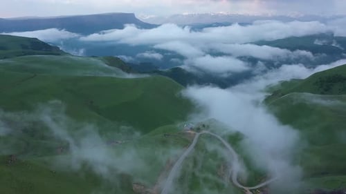 Aerial view on the green fields at the mountains in the clouds and fog