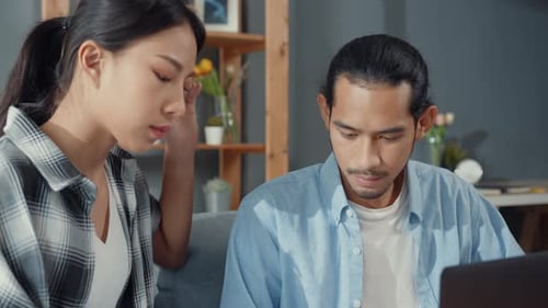 Asia young couple man and woman sit on couch serious focus on laptop computer check document paper.
