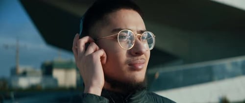 Jovem com óculos ouvindo música segurando seus fones de ouvido