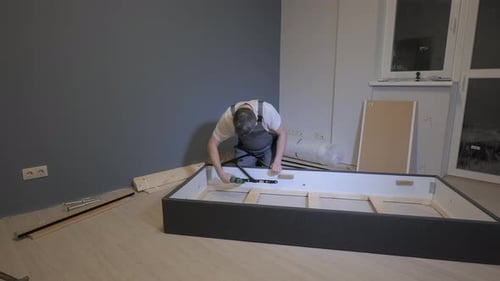 Un constructeur en combinaison de travail assemble un lit dans un nouvel appartement