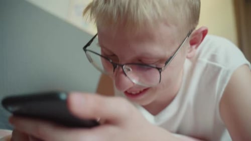 Focused Child Using Smartphone Lying Down Indoors