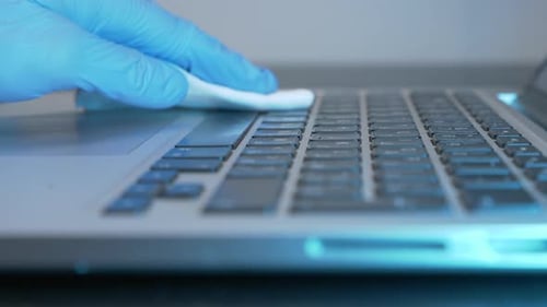 Female hand is rubbing laptop computer with sanitizer and wet wipe in office during quarantine.