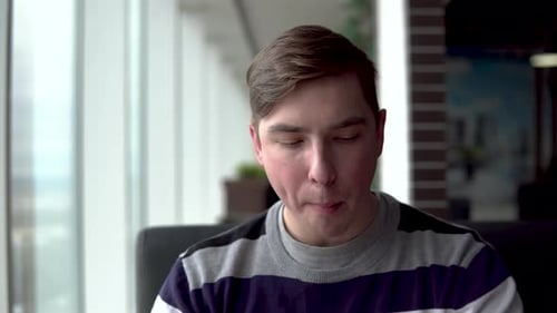 A Young Man Is Eating a Burger. A Man Sits in a Cafe By the Panoramic Window and Eats Fast Food.