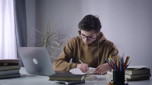 Fokussierter kaukasischer Junge, der im Lehrbuch schreibt und auf den Laptop-Bildschirm schaut. Porträt der Konzentrierten