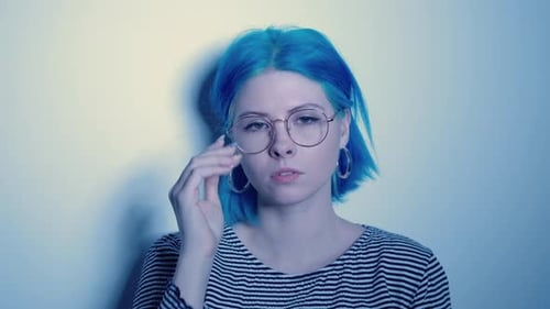 Stylish Young Woman with Blue Hair Puts on Glasses