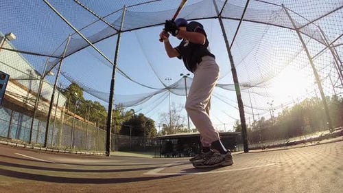 A baseball player practicing at the batting cages.