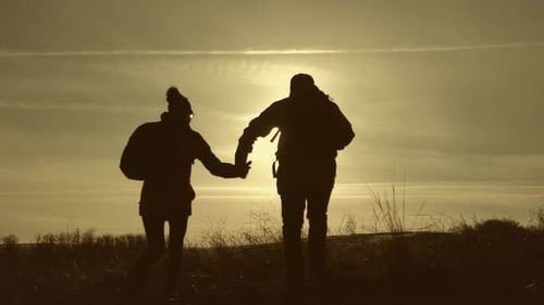 Silhouetten von zwei Wanderern mit Rucksäcken, die den Sonnenuntergang von der Spitze eines Berges genießen