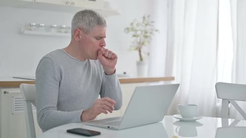 Gray Haired Man Coughs While Using Laptop at Home