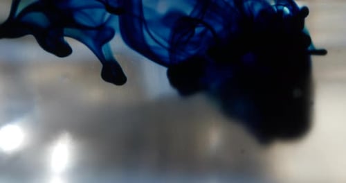 Makroaufnahme eines blauen Tintentropfens in klarem Wasser, während er sich unter Wasser ausbreitet und eine rauchige abstrakte