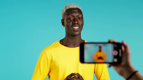 Lächelnder afrikanischer Blogger-Mann macht online neuen Videoblog, Vlog, mit seinem Smartphone auf Blau