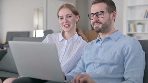 Fröhliches junges Paar tätigt Videoanruf auf Laptop zu Hause