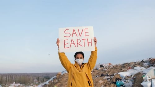 Young Adult Holding Save Earth Sign at Landfill