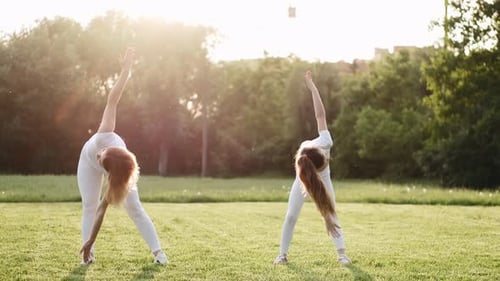 Woman and Girl Doing Yoga Stretches in Park