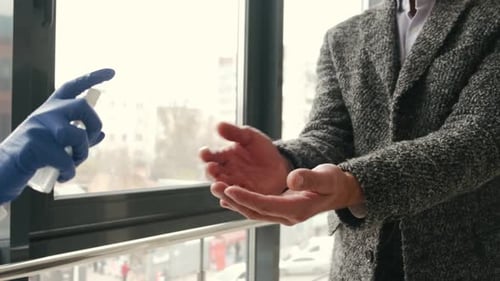 Airport Worker in Protective Equipment Disinfecting Male Hands with a Spray
