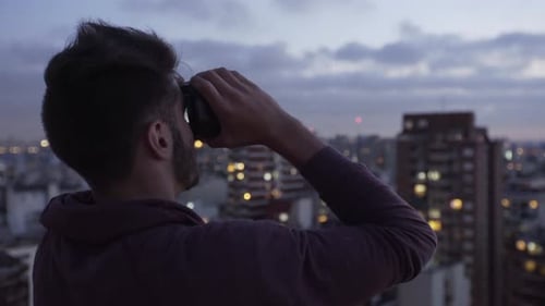 Man Using Binoculars On Rooftop Overlooking City at Night
