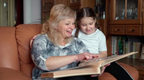 Senior 60s woman with granddaughter looking at old photo album close-up