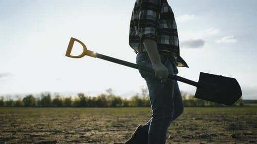 Person Carries Shovel Across Rural Agriculture Field