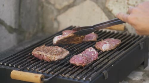Man Flips the Grilled Steak with Tongs