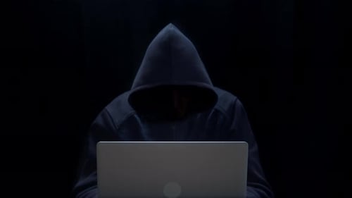 Figure in Hoodie Typing on Laptop in Dark