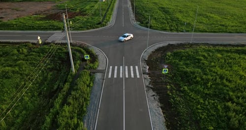 Car Travels Along Crossroads Road in Green Field