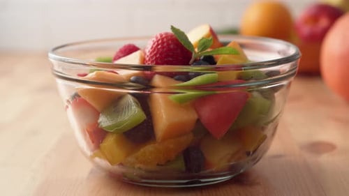 Camera follows putting fresh mint over fruit salad. Slow Motion.