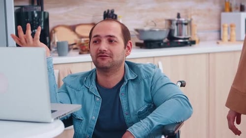 Man in Wheelchair Video Calling on Laptop in Kitchen