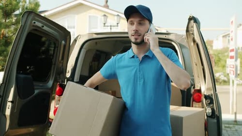 Delivery Man Talking on Mobile Phone Holding Parcel Standing Near Commercial Van Outside
