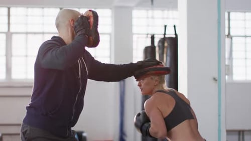 Caucasian female boxer wearing boxing gloves training her punches with male trainer at the gym