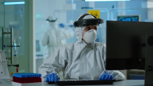 Researcher in Protective Suit Typing on Computer