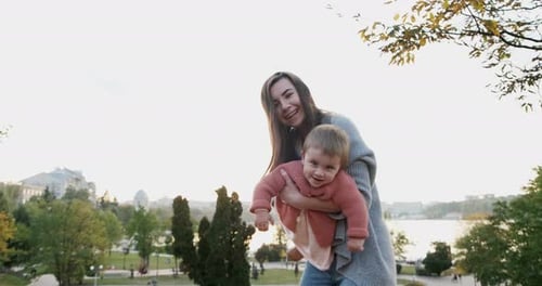 Pretty Young Woman Holding Baby Girl in Her Arms at Sunset at Park, Happy Mother Playing, Hugging