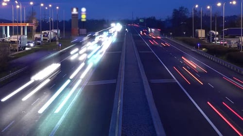 A Time Lapse of Busy Highway with Gas Station on One Side and Parking Lot on Another Side at Night.