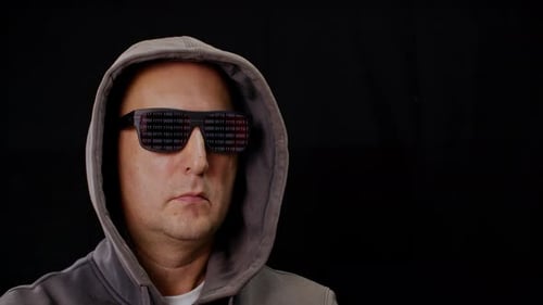 Computer Hacker en sweat à capuche et lunettes de soleil noires reflétant le code binaire sur fond noir.
Homme