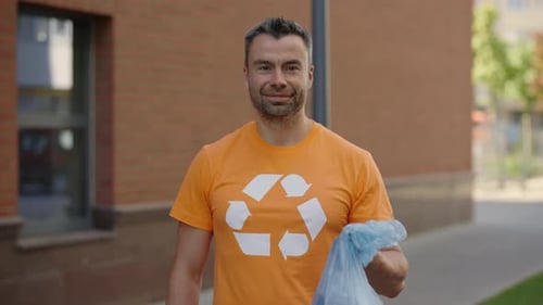 Retrato de hombre voluntario de pie y sosteniendo una bolsa de basura con basura clasificada mirando a la cámara
