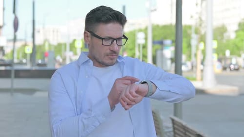 Man Using Smartwatch on City Street, Daytime