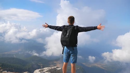 Hiker with Backpack Standing on Mountain Edge and Raising His Hands Enjoying Freedom. Man Actively