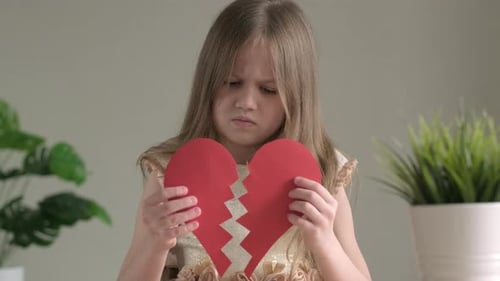 Sad Girl Holding Torn Paper Heart Indoors