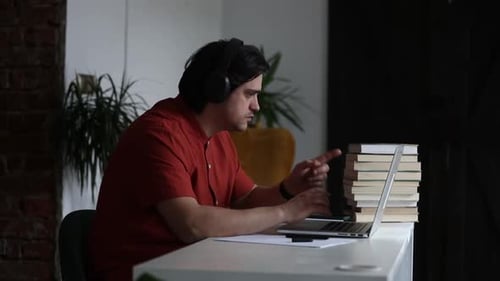 Man working at home office at laptop and listen a music in headphones