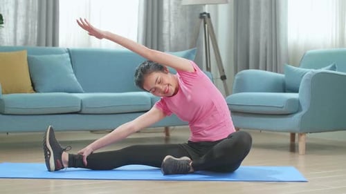 Woman Stretches Arm While Sitting on Exercise Mat