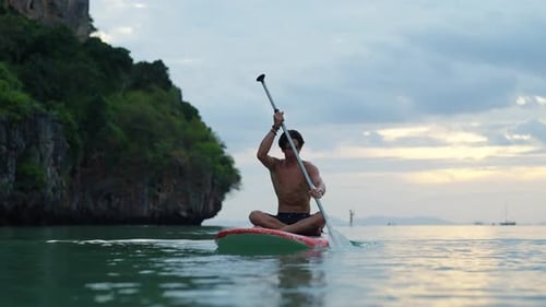 4K Young Asian man paddleboarding in the sea at summer sunset.