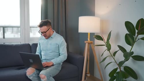 Man Reacts Expressively at Laptop on Couch Indoors