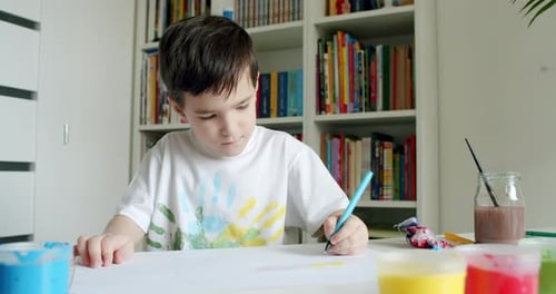 Boy Draws with Pen at Desk