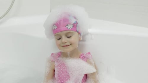 Jolie fille blonde prend un bain en maillot de bain. Un petit enfant se lave la tête