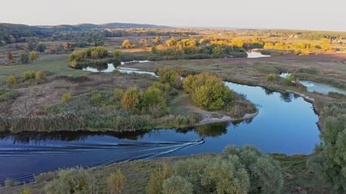 Small Motorboat Sails on Long Curvy River Running on Meadows