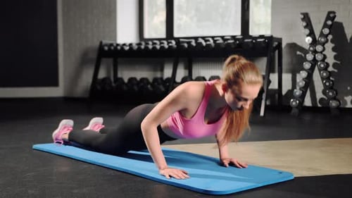 Young woman has workout at gym. Standing on knees and doing push ups with strong hands