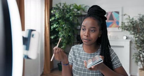 Artista de maquillaje experimentado de ascendencia afroamericana aplica sombra de ojos en los párpados grabando un