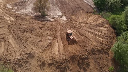 Aerial view of bulldozer flattening surface on further construction site