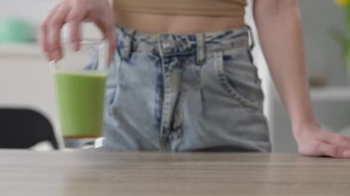 Front View Female Hand Throwing Vitamins Off Table Putting Green Healthful Smoothie in Glass